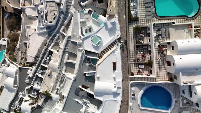 Spectacular drone video soaring above Santorini&rsquo;s iconic white Cycladic rooftops, sunlit infinity pools, and winding stone walkways, with sweeping seaside vistas in crisp daylight aerial footage.