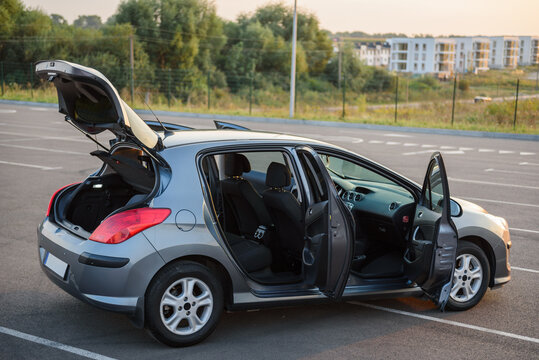 Modern gray hatchback car with open doors and trunk parked in an empty parking lot during a sunset evening. Exterior view of the vehicle outdoors.