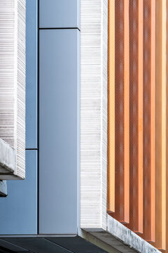 Between pale surfaces, blue panels align with orange fins as modern architecture turns the vertical facade into a geometric detail of layered texture