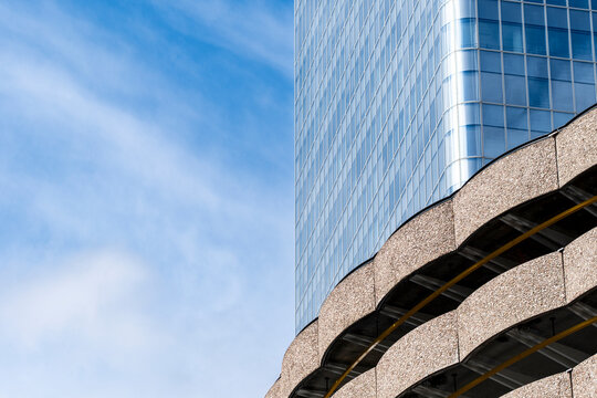 Against an open sky, sweeping lines lead from brutalist concrete toward a curved glass facade, where modern architecture sharpens urban contrast