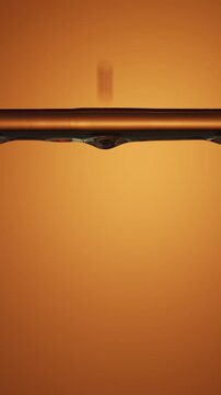 Continuous dripping of transparent essence on warm orange background macro