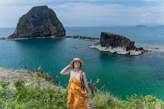 Woman in orange dress admiring twin sea stacks, Hon Yen, Dak Lak, Vietnam