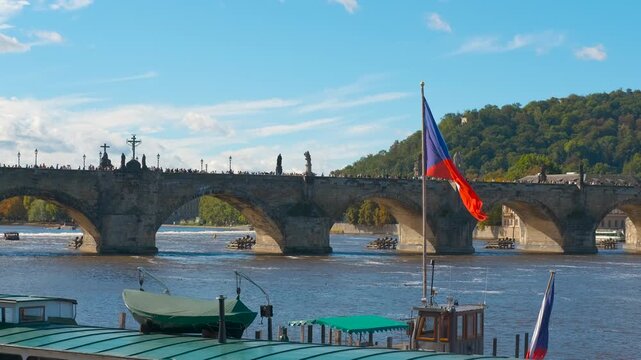 Czech flag waving on river in Prague. Red, white, and blue czech flag waving in the wind from a boat on the vltava river, with the historic charles bridge and its statues visible in the background