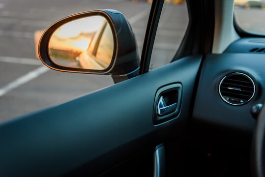 Left side rearview mirror inside a car. Close-up view of the vehicle's exterior left mirror and interior driver side panel during sunset.