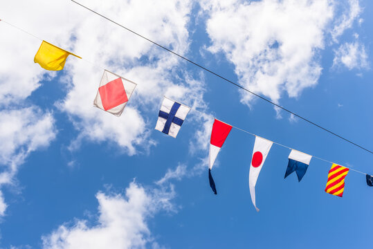 Colorful maritime signal flags displayed on a rope against a bright blue sky with scattered white clouds. A nautical communication concept ideal for marine, sailing, travel, and commercial use.