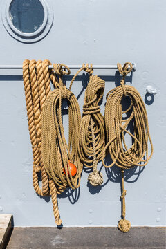 Ropes on an old transport ship, neatly coiled and hanging from a metal bar beside a porthole, showing maritime equipment, nautical craftsmanship and the textured surfaces of a working vessel.