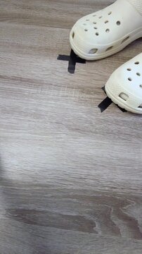 Two shoes aligned on tape marker on wood floor, matching crocs placed over black tape cross, confirmed foot placement for rehearsal or dance, sense of stability and coordination,