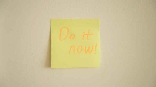 A woman puts a sticker do it now on white wall