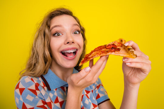 Happy teenage girl with braces enjoying a slice of pizza against a bright yellow background