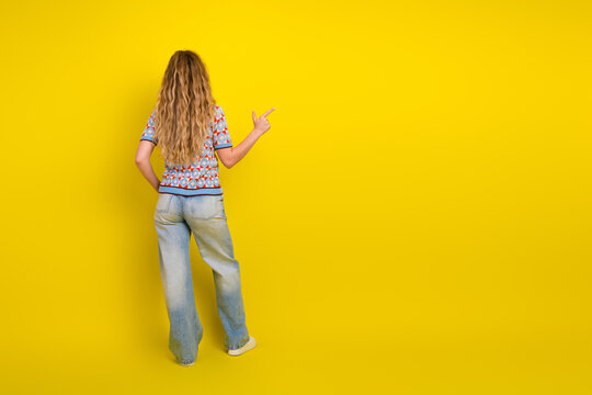 Young woman back view pointing to empty yellow background with long hair and casual jeans perfect for advertisement, concept, and directional gesture in studio mockup and copy space