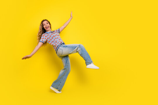 Happy young woman jumping with joy on a bright yellow background, casual jeans and sneakers showing playful energy, freedom and retro casual fashion in a colorful studio portrait
