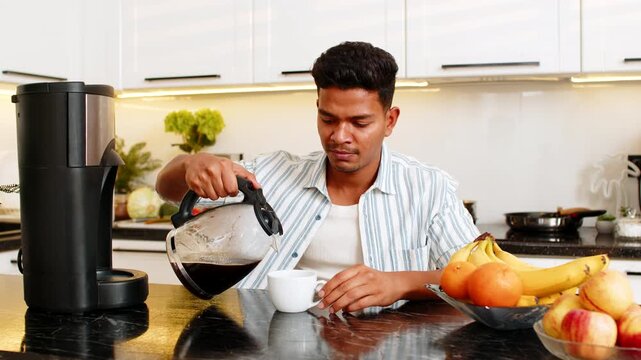 Indian man pouring fresh coffee into cup in home kitchen and enjoying rich aroma during quiet break. Arabian guy smiling over warm drink for cozy leisure break and peaceful breakfast routine indoors.