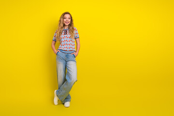 Fototapeta premium Smiling teenage girl in casual retro sweater and wide jeans standing against a bright yellow background, confident relaxed pose and cheerful fashion portrait