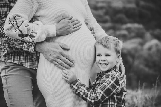 Black and white photo family in autumn. Family portrait outdoors in autumn. A pregnant woman, man, and their little son standing together on a scenic hill with a forest background, embracing.