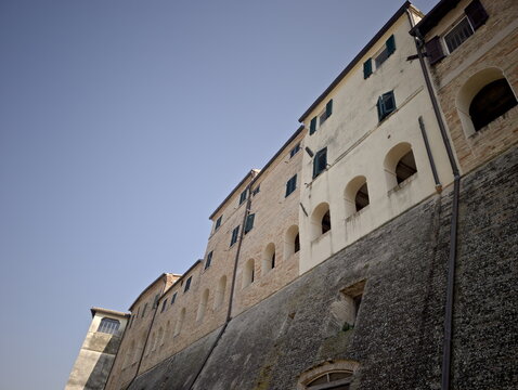 Edificio storico in pietra e intonaco ripreso dal basso, con finestre ad arco, persiane scure e struttura elevata su base in pietra