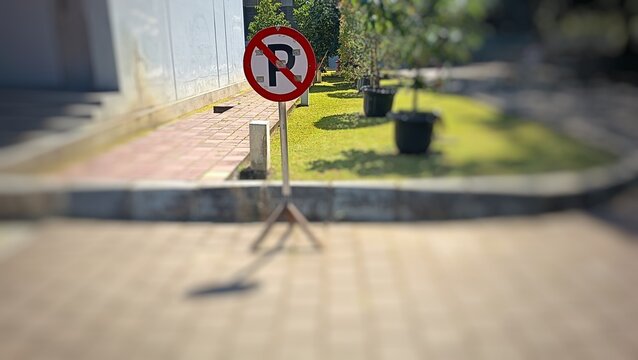 No parking traffic sign standing in an outdoor public area with blurry background pavement and landscape.