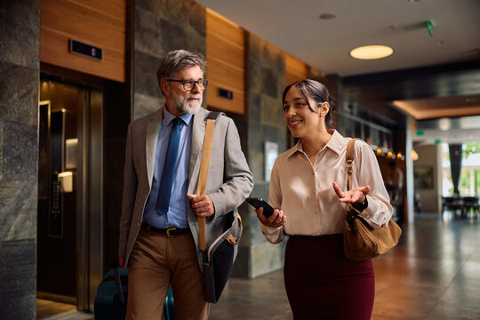 Happy businesswoman communicating with mature colleague walking through hotel.