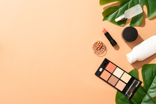 Summer make up background. Shadow palette, lipstick, serum bottle with palm leaves.
