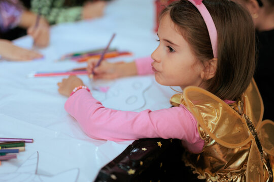 Fairy Costume Little Girl Drawing With Pencil At Kids Party. Creative children wearing butterfly wings sketches together on paper during festive birthday workshop