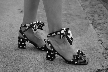 Close-up of a woman wearing black and white polka dot high heel sandals while standing outdoors. Fashion footwear detail captured in black and white with a stylish and elegant composition. © pixarno