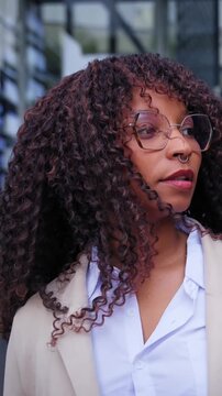 Vertical. Black Latina professional leaving a modern office while passing other employees near the entrance. Candid corporate scene showing commuting, diversity and everyday workplace life.