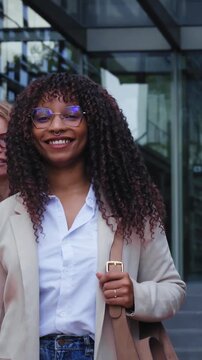 A vertical group of cheerful young professionals walks forward outside a contemporary corporate venue. They are smiling and looking at the camera during a bright daytime work break