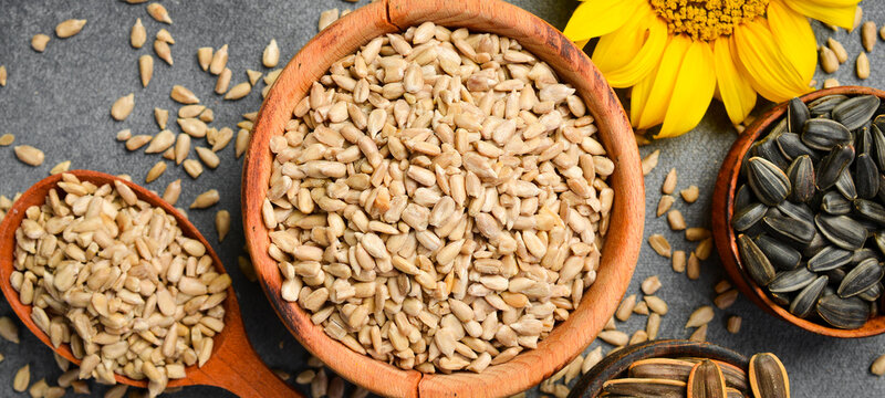 Peeled sunflower seeds rest in a wooden plate on a dark background. Natural organic kernels offer high nutrient value. Great choice for healthy diet concept.