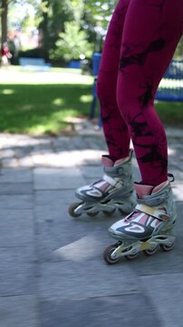 Vertical screen close up view of female legs in roller skates gliding on a park path showing wheel movement balance and recreational inline skating on a sunny summer ride