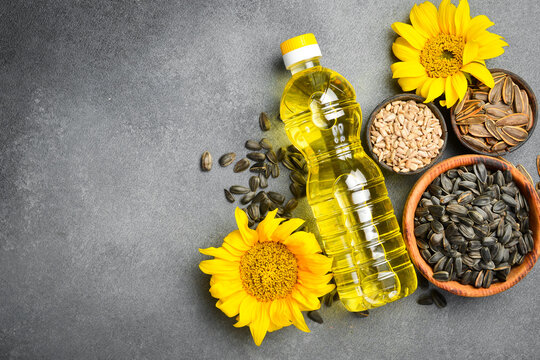 Plastic bottle of golden sunflower oil rests near yellow flowers and bowls with seeds. Essential organic kitchen ingredient. Ideal background for food product advertisement.