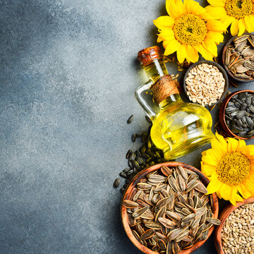 Sunflower oil in a glass jug rests with flowers and raw seeds on dark background. Essential organic cooking ingredient. Perfect image for healthy food product advertisement.