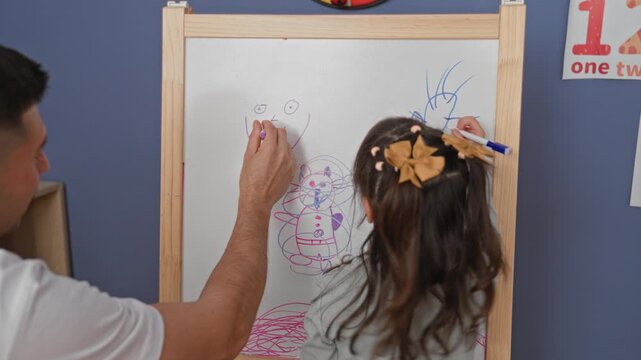 Child draws on whiteboard with marker while teacher guides with hand at the board in a school building; creative learning curiosity.