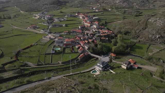Drone footage capturing Albergaria da Serra from above, with terraced fields, grazing pastures, and historic village buildings surrounded by nature. Drone rotating to the left.
