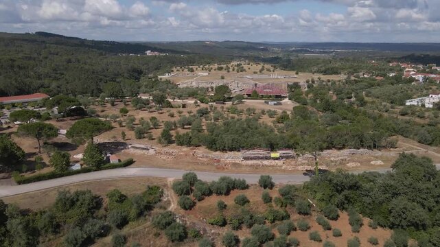 Cinematic aerial drone footage capturing the reconstruction of Con&iacute;mbriga&rsquo;s outer defensive wall, with workers restoring ancient Roman stonework in a historic archaeological setting.