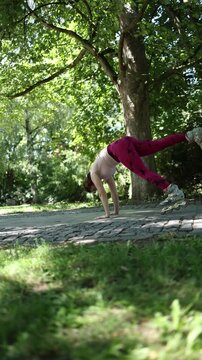 Vertical screen woman performs a dynamic donkey kick on rollerblades balancing on her hands in a park combining skating with a playful acrobatic fitness challenge outside