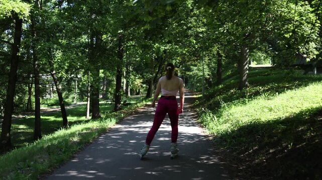 Woman rollerblades alone along a shaded park path enjoying smooth movement fresh summer air and active recreation while exploring a peaceful green urban environment on wheels