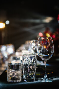 Elegant table setting with glassware, wine glass and decorative tumblers on a black banquet table. Sophisticated event setup, luxury style, bokeh background, perfect for wedding or party.