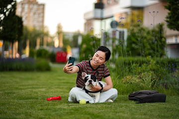 Fototapeta premium Japanese woman taking selfie with French bulldog in park