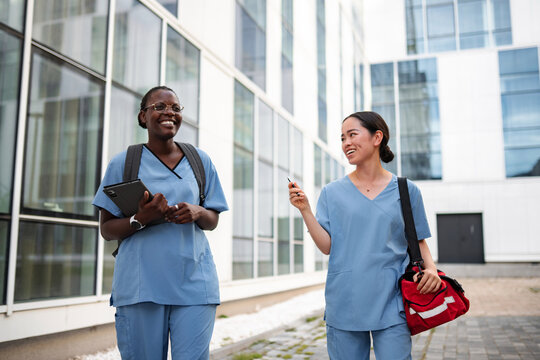 Diverse nurses walking enjoying conversation outside clinic building