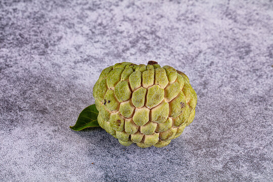 Fresh ripe custard apple or sugar apple with leaf on textured grey background