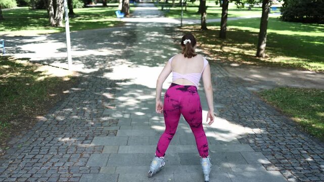 Woman wearing inline skates hesitates at the top of a gentle downhill path as a complete beginner preparing to make her first careful descent while overcoming fear and uncertainty