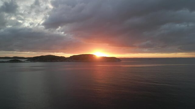 Aerial panning shot of the sun setting over the ocean horizon with golden sun glitter shimmering across the water.