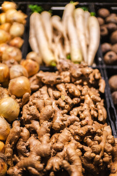 Fresh ginger roots with onions and white radish displayed in supermarket vegetable section with organic produce and healthy cooking ingredients