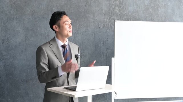 グレー背景でプレゼンをするスーツを着た日本人男性