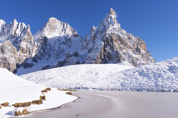 Winter landscape featuring snow-capped mountain peaks and a frozen lake under a clear blue sky. High-altitude wilderness scenery for travel and nature themes. © marcodenaro
