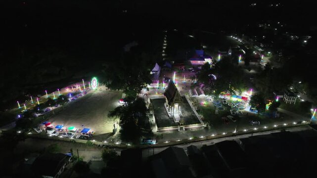 Dazzling colorful lights illuminate the traditional Thai temple fair in Nong Bua Lamphu at night. Experience the vibrant ambiance and cultural energy captured from an aerial perspective.