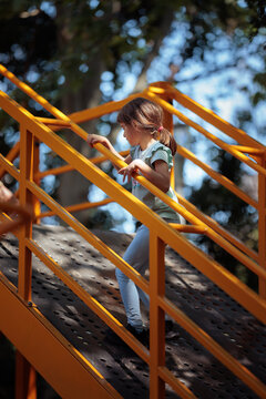 Active Little Girl Climbing Metal Ramp At Outdoor Children Playground. Brave child scales steel playground structure exercising her motor skills during sunny day
