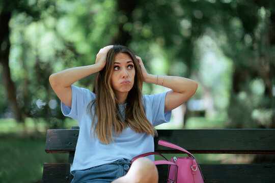 Exasperated Woman Sitting On Park Bench Holding Her Head Outdoors. Stressed frustrated female cries alone outside covering face during emotional personal crisis breakdown