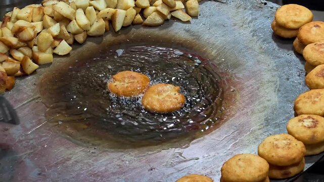 Indian street vendor frying aloo tikki on large iron griddle