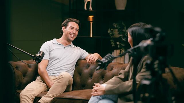 Friendly male guest speaker talking with a female host during a live broadcast. Two people recording a podcast in a professional studio