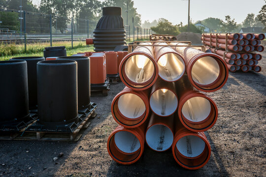 Stacked Orange Sewer Pipes and Black Manhole Chambers in Construction Yard